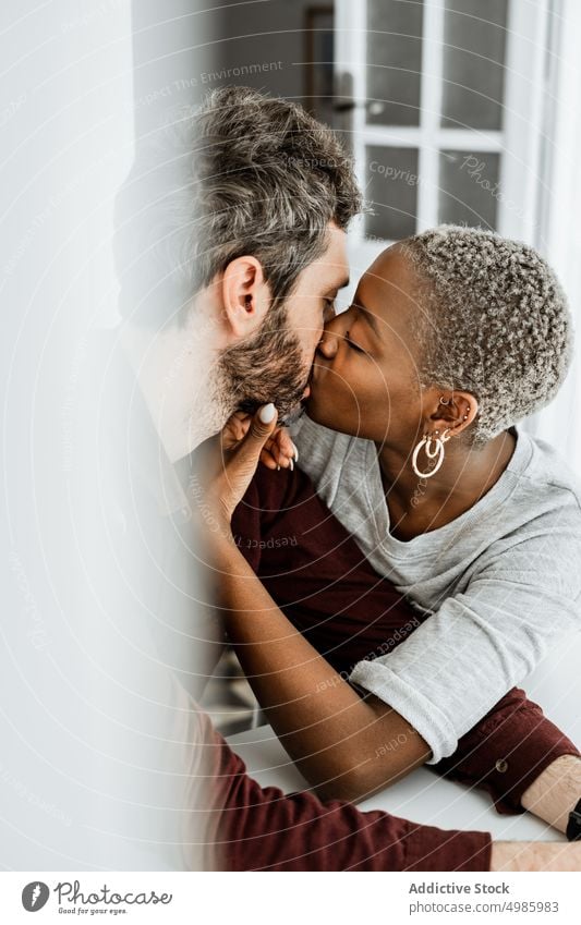 Young multiethnic lovers during tender kiss at table couple home relationship casual sit hug cuddle embrace together romantic affection african american black