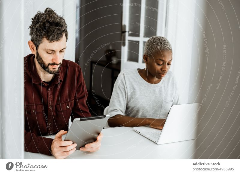 Smart multiethnic couple using gadgets at home laptop device busy addict digital sit table browsing watch apartment kitchen modern black african american