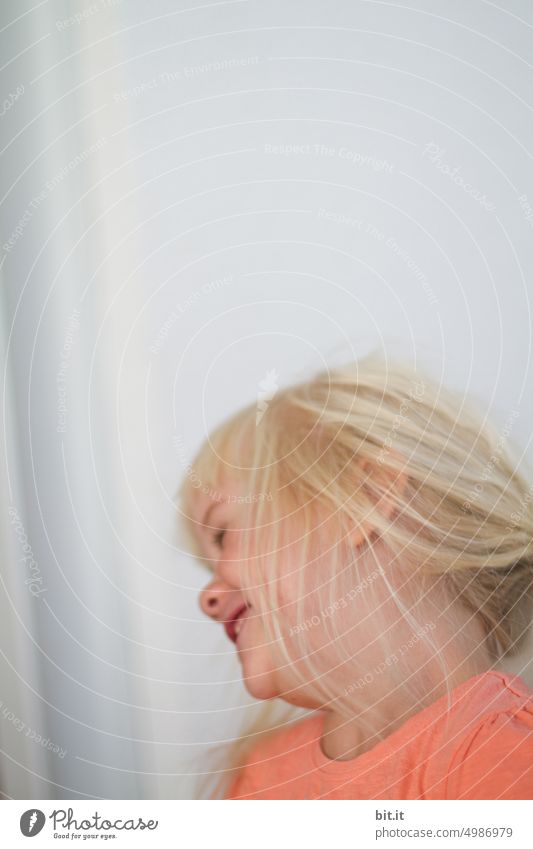 Throwing myself away. Natural blonde girl against light neutral background, in half profile moves and laughs. Child, girl from the side in motion. Funny, funny portrait with motion blur. Childhood, happiness, cheerfulness, humor.