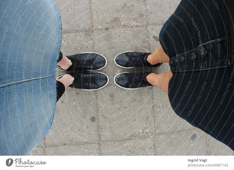 Two pairs of black sneakers and two denim skirts; two women face each other, bird's eye view Black sneakers Denim skirts feet Footwear from on high Stone slab