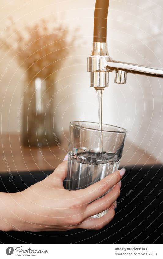 Woman filling drinking glass with tap water on the kitchen. Concept of clean drinking tap water at home. Pouring fresh drink. Water quality check concept. The concept of saving, problems with water