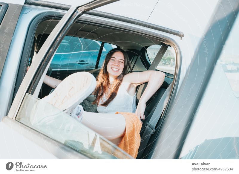 Young woman resting on the back seats of a car smiling during a sunny day. person enjoyment freedom journey wind window passenger sitting sunlight fun
