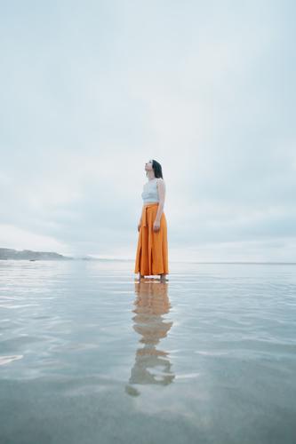Woman standing on trendy clothes on the beach while reflecting on the water carefree energetic freedom joy positive active fun happy ocean sun woman young boho