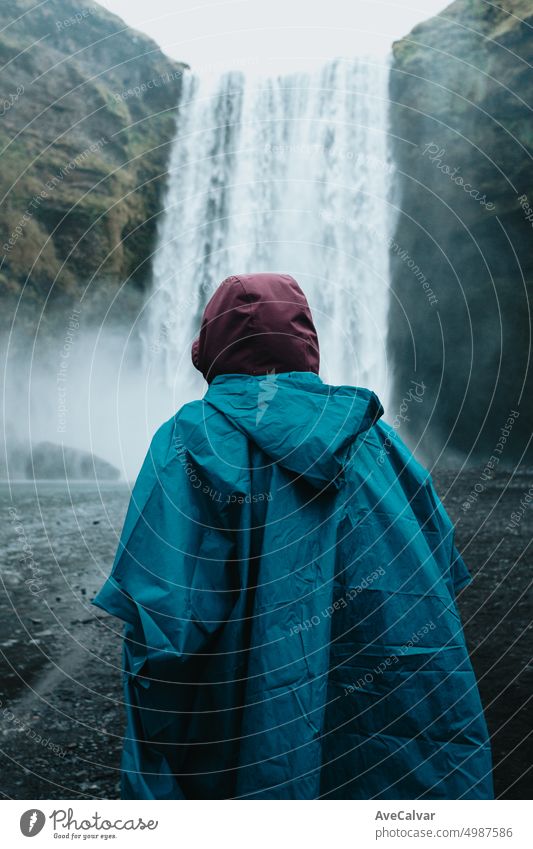 Young traveler in front of massive skofagoss waterfall at Iceland Island during a foggy rainy day person woman exploration horizontal majestic standing
