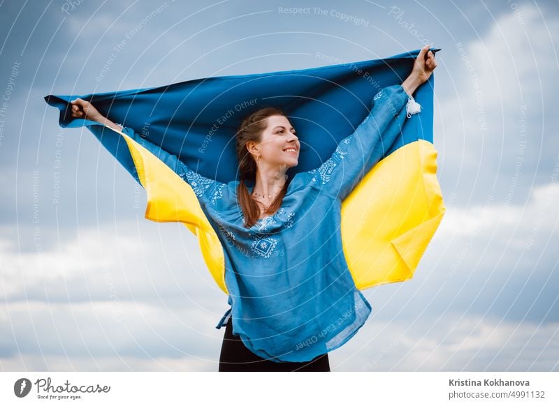 Happy free ukrainian woman with national flag on dramatic sky background. Portrait of lady in blue embroidery vyshyvanka shirt. Ukraine, independence, patriot symbol