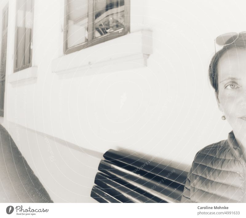 Frau sitzt wartend auf einer Sitzbank einer Bahnstation an einer Hausfassade Gesicht portrait lifestyle lächeln lachen gesicht freizeit glücklich hübsch