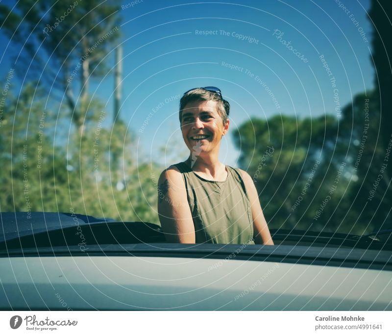 Frau schaut lachend aus einem Autodach heraus glücklich lächeln portrait schön hübsch lifestyle erholung urlaub reise freizeit sonne Natur sommer Freiheit