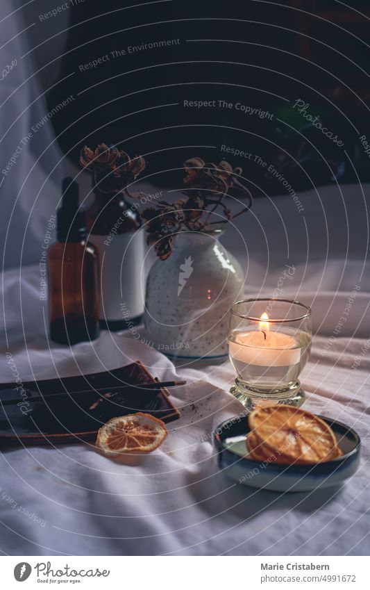 Vertical shot of essential oil bottles, dried lemon slices and a tea candle for a cozy autumn mood spa setting Dark Candlelight Wellbeing Autumn Hygge