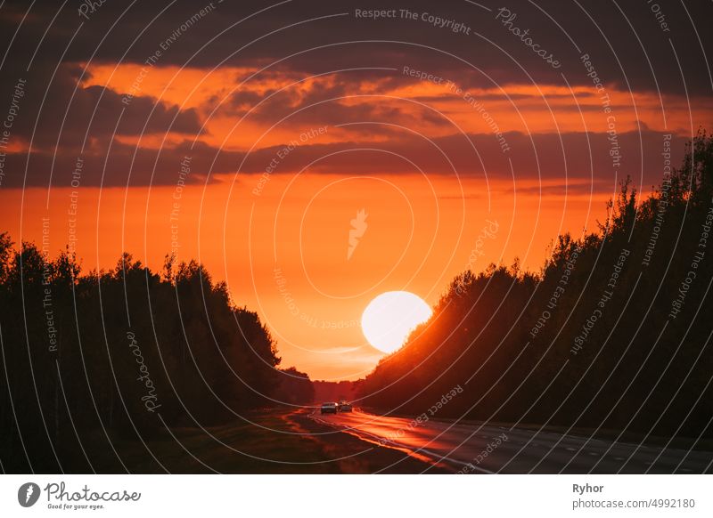 Cars In Motion On Road, Freeway. Asphalt Motorway Highway Against Background Of Big Sunset Sun. Travel Trip Concept. Sunshine Above Road beautiful bright car