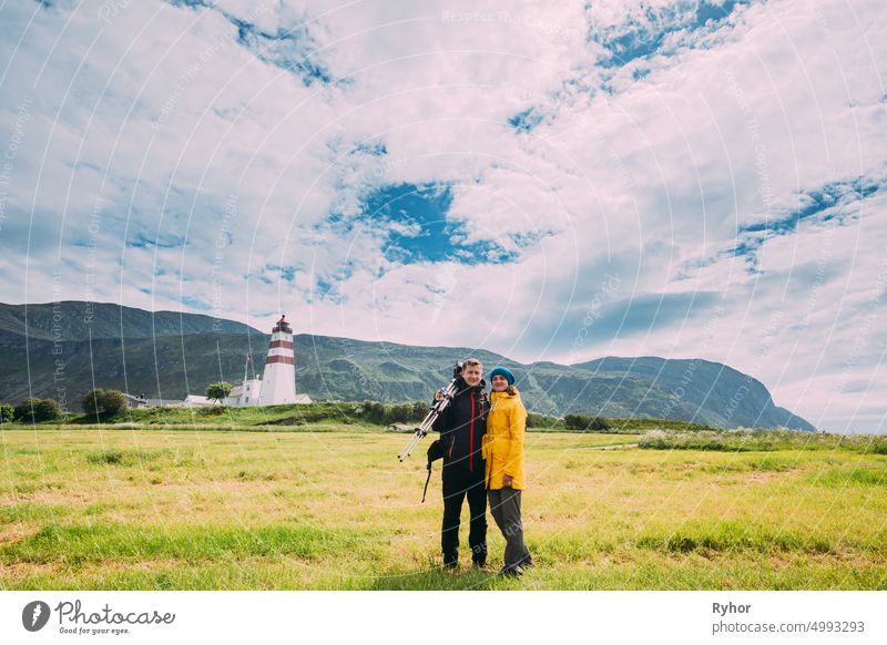 Alnesgard, Godoya, Norway. Man And Woman Young Adult Caucasian Tourists Travelers Couple Posing Against Old Alnes Lighthouse In Summer Day In Godoy Island Near Alesund Town. Alnes Fyr