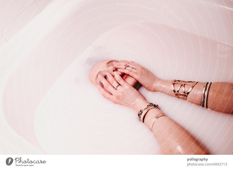 Eine Frau taucht in der Badewanne unter milchiger Flüssigkeit, bedeckt das Gesicht mit Händen Selected blurry products woman face artistic hands badewanne