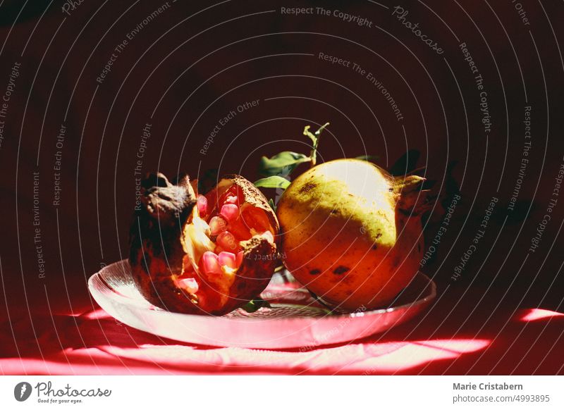 Vertical shot of light and shadows cast on two pomegranate fruit in a glass platter showing an autumn theme background and aesthetic Pomegranate Autumn Red