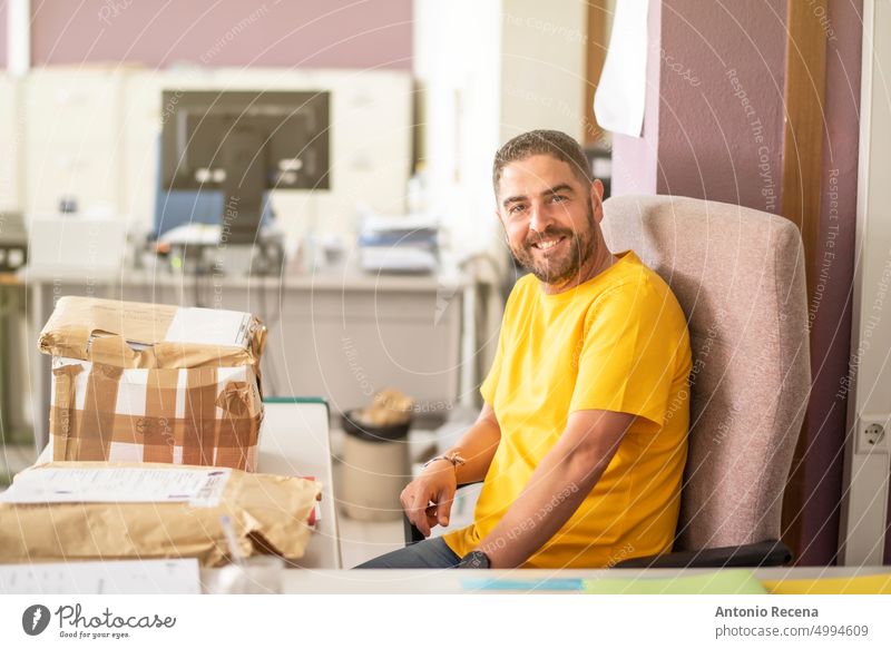 Office man smiles at camera in charge of packing packages parcel shipping programmer computer office worker clerk file real people latin attractive white collar