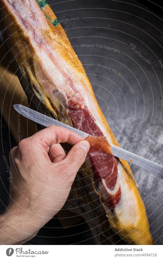 Faceless chef cutting delicious ham leg with knife jamon pork delicacy meat protein slice tasty tool nutrition natural dry cured product organic big size