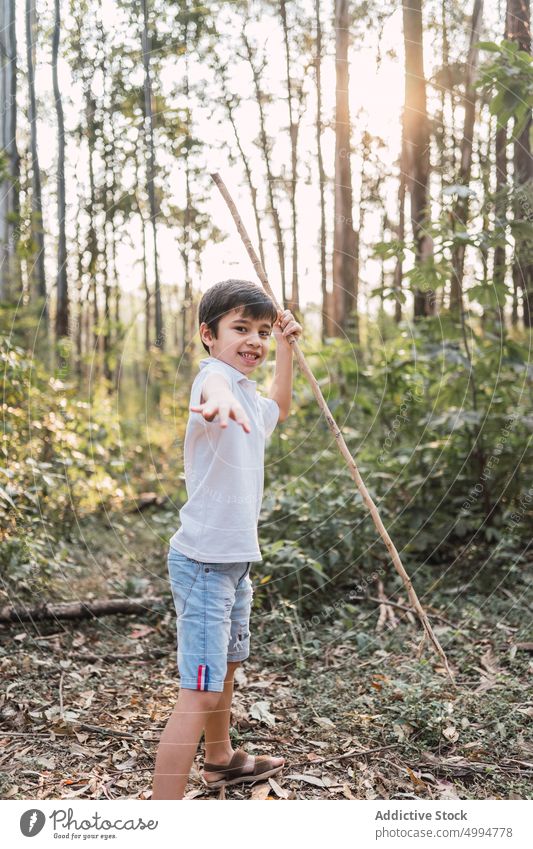 Smiling boy with twig in summer forest outstretch smile childhood sincere friendly nature portrait denim shorts t shirt woods content charming pleasant stand