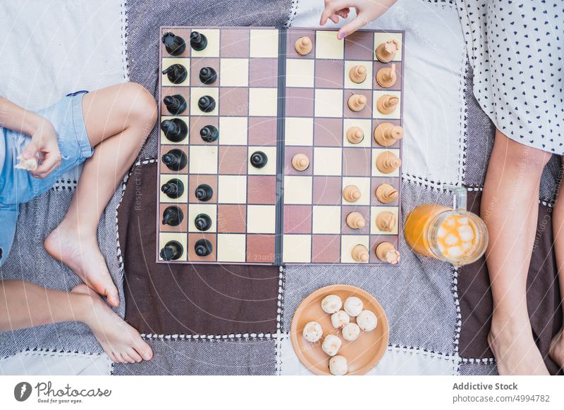 Anonymous siblings playing chess on plaid during picnic on meadow recreational sport drink biscuit spend time lawn sister brother childhood children kid fabric