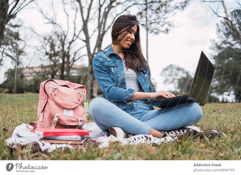 Happy woman using laptop in park student education exam preparation study online campus young female ethnic hispanic denim jeans homework browsing internet