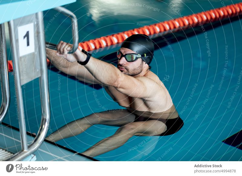 Swimmer in goggles and cap exercising in pool athlete sport workout stretch swimming exercise warm up man sportsman training block outstretch pure water number