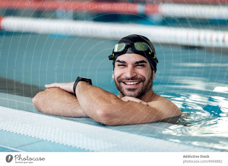Smiling swimmer in goggles leaning on poolside smile lean on hand sincere friendly masculine man portrait athlete cheerful content sport macho tired accessory