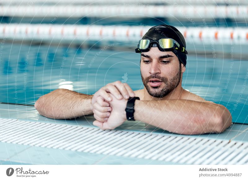 Swimmer in goggles checking up time on wristwatch in pool swimmer check up masculine macho man portrait accessory attentive athlete watching swimming sportsman