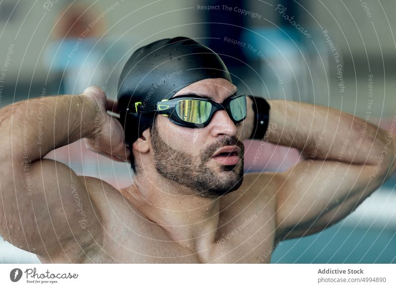 Muscular swimmer in goggles and cap against pool athlete hand behind head bicep sporty masculine macho man portrait brutal triceps shirtless muscle accessory