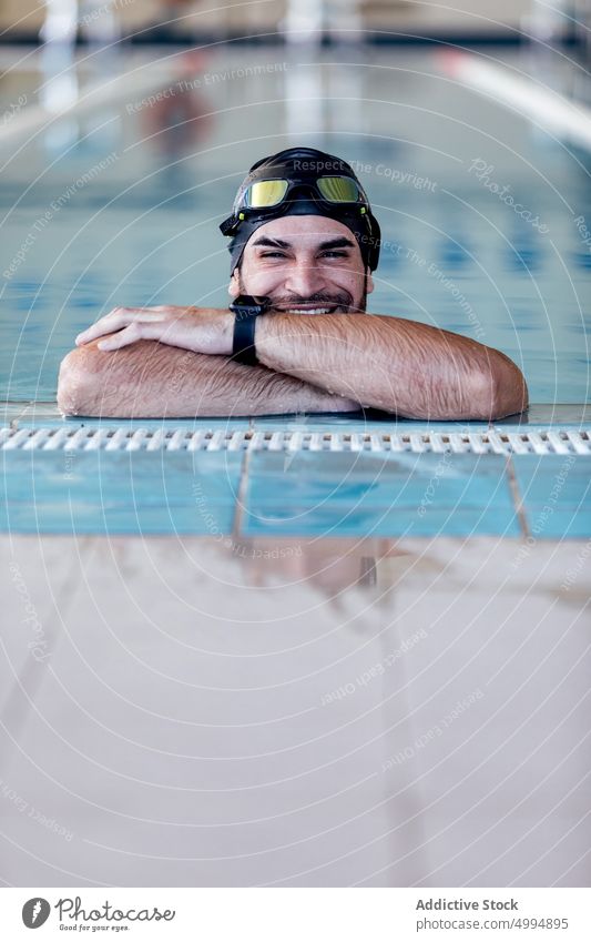 Smiling swimmer in goggles leaning on poolside smile lean on hand sincere friendly masculine man portrait athlete cheerful content sport macho tired accessory