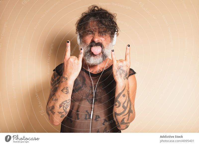 Bearded man showing rock gesture and listening to music rocker rebel tongue out rock and roll horn male mature middle finger gray beard headphones grimace