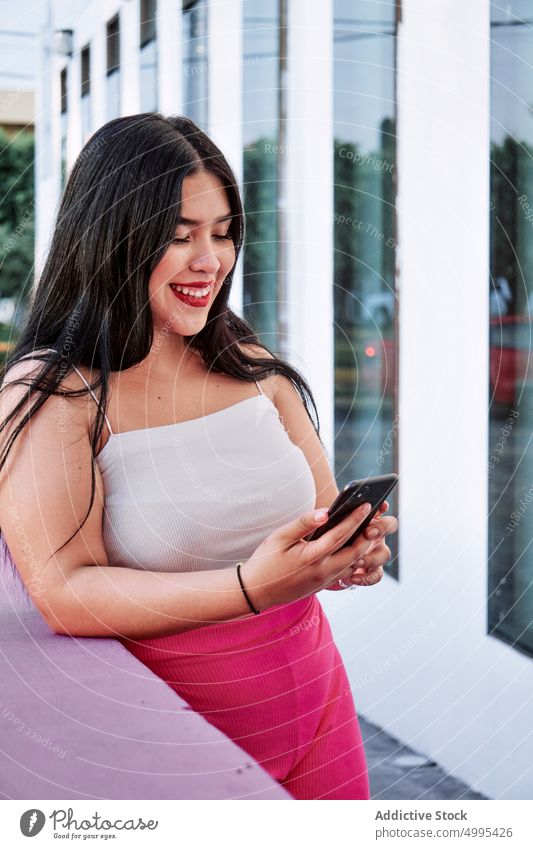 Plus size female browsing cellphone woman watching smartphone street lean border smile urban style ethnic mobile cheerful positive optimist glad overweight