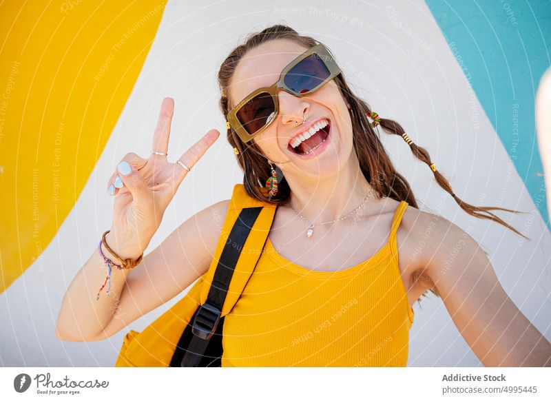 Happy female taking selfie on street woman happy funny modern urban v sign two fingers sunglasses grimace style young cheerful backpack memory tourist traveler