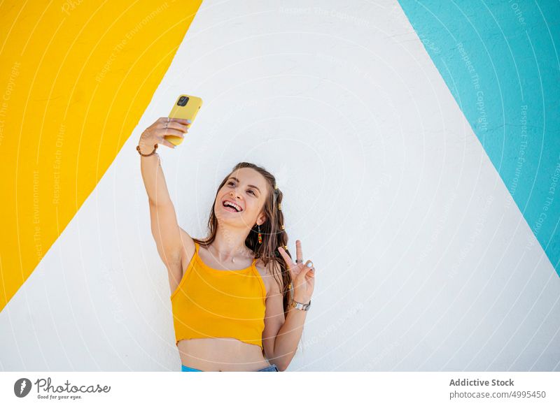 Young woman gesturing V sign and taking selfie smile v sign smartphone wall street weekend happy bright female young style summer cellphone gadget cheerful