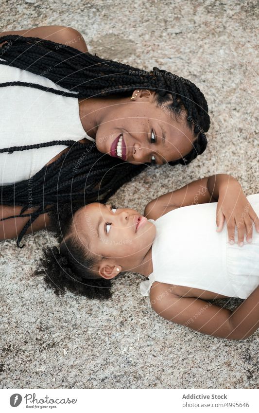 Cheerful African American mother and daughter on ground smile happy group weekend together love stone woman girl black african american ethnic afro braids