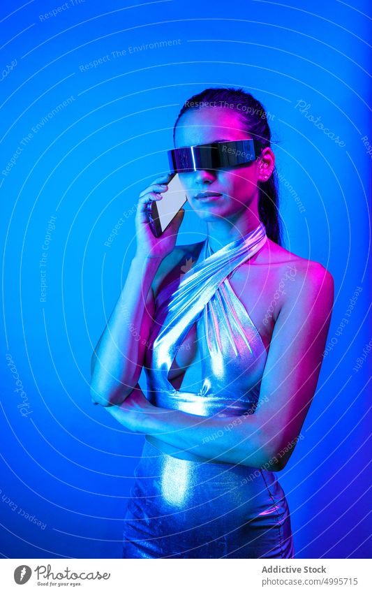 Serious futuristic woman having phone call in blue studio virtual reality smartphone style experience confident talk vr communicate cyberspace digital female