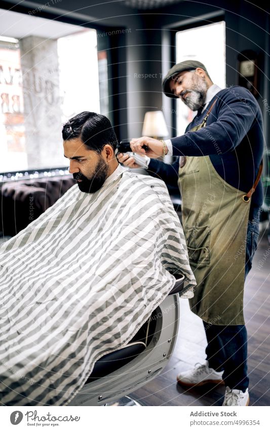 Client getting haircut in modern barbershop client salon hispanic grooming ethnic cape customer professional men service male hairstyle treat master procedure