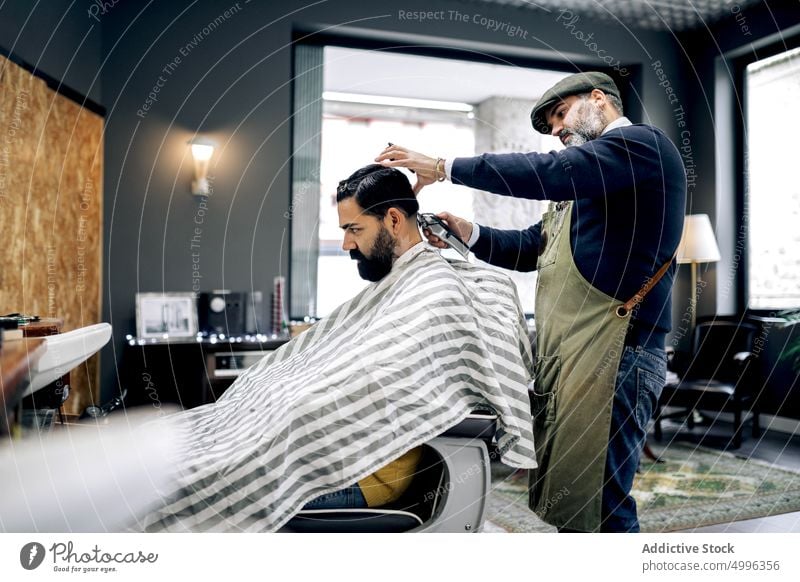 Client getting haircut in modern barbershop client salon hispanic grooming ethnic cape customer professional men service male hairstyle treat master procedure