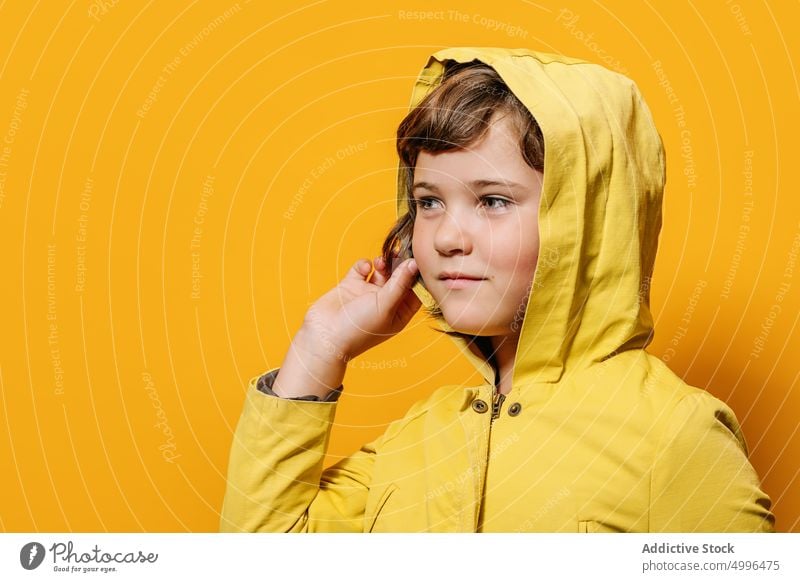 Girl looking at camera against yellow wall in studio girl colorful style autumn portrait childhood raincoat little vivid kid jacket winter hoodie trendy outfit