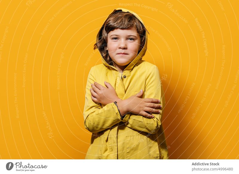 Calm boy in trendy outfit standing with crossed arms against yellow background hug calm embrace childhood style individuality arms crossed wear self hug kid
