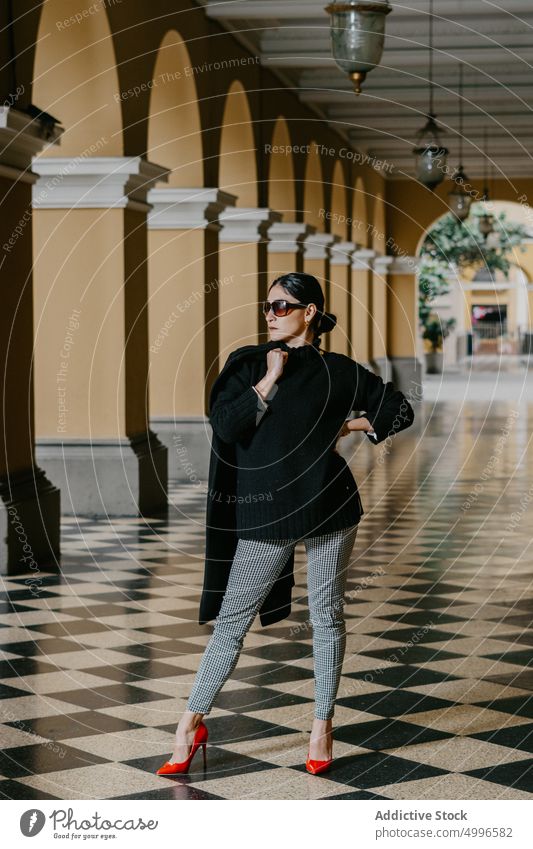 Confident young ethnic woman standing in arched passage with hand on waist confident style gorgeous serious outfit model feminine personality female hispanic