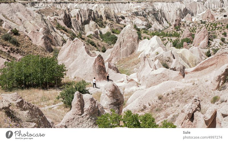 Two people in a wide volcanic formed stones in Cappadocia trekking way Landscape following - movement activity Walking Lost sunny day Colour photo