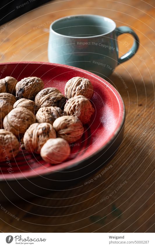 Walnuts in a red ceramic bowl on a wooden table with a light blue cup in the background Clay bowl red shell Wooden table Cup Cup with handle Mint green