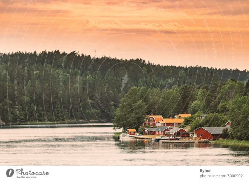 Sweden. Many Beautiful Red Swedish Wooden Log Cabins Houses On Rocky Island Coast. Lake Or River Landscape apartment archipelago bathhouse beautiful building