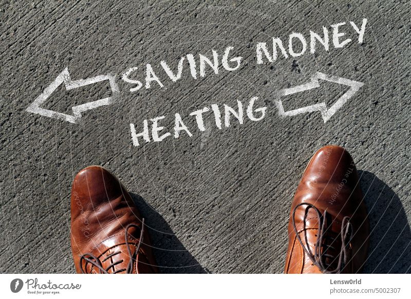 Person having to decide between Heating and Saving Money - top view of the words and arrows pointing in opposite directions business choice concept