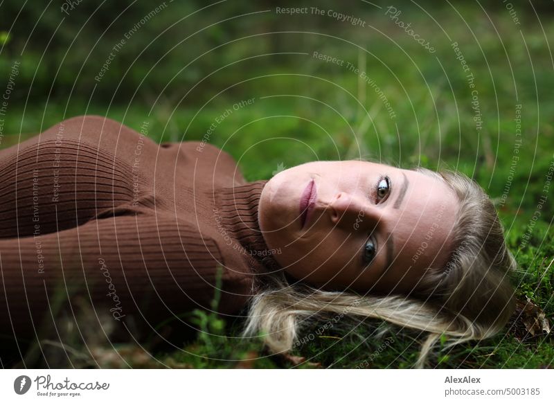 Young blonde woman with dimples lies on the moss in the forest and looks at the camera from the side Young woman Woman Blonde Feminine pretty fortunate