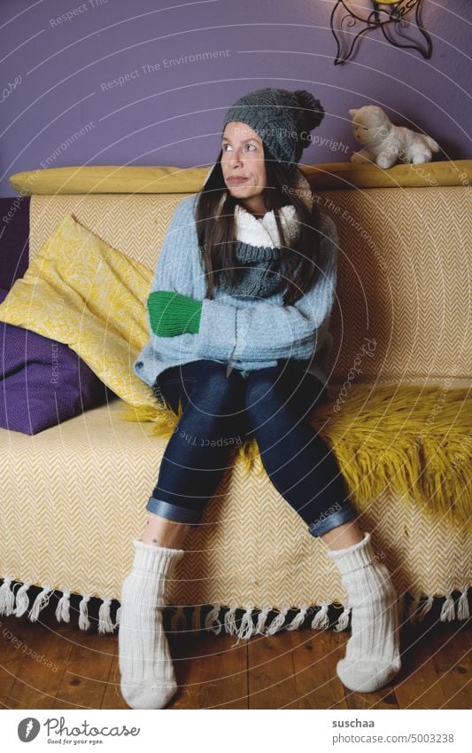 woman sitting on the sofa and shivering to herself Woman frozen Cold Flat (apartment) at home Winter Heating off Energy crisis Save energy Save heating costs