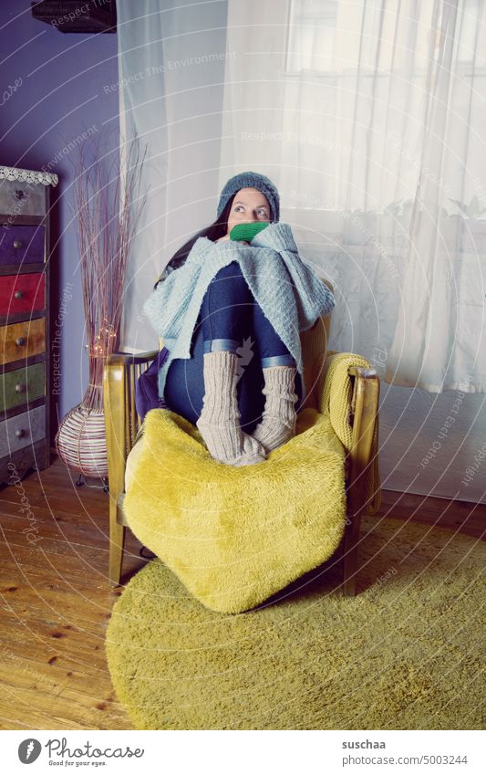 woman sits on an armchair with woolen clothes and still freezes Woman frozen Cold Flat (apartment) at home Winter Heating off Energy crisis Save energy