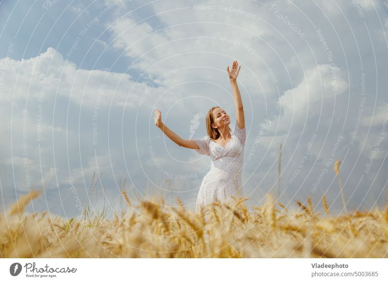 Young woman in summer dress dancing alone in ripe wheat field basket hat back view rye hair blonde wicker blue elegant rustic country nature freedom beautiful