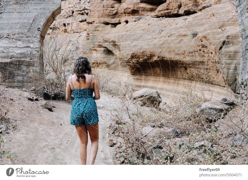 Woman walking by a dried canyon woman tourist nature visiting travel hiking blue copy space dress river desertic dry volcanic rocks dirt country tenerife rural