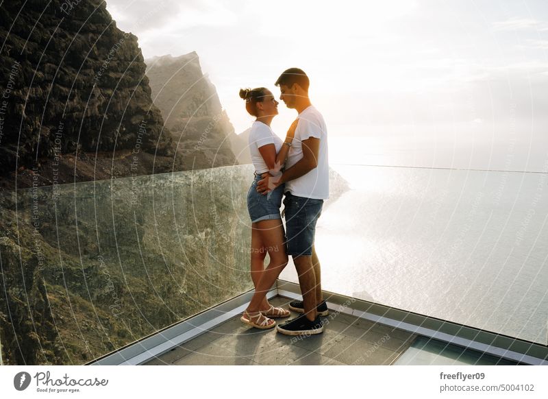 Young couple on a viewpoint against volcanic cliffs and the ocean love honeymoon young sunset caucasian copy space rocks canary islands spain sea black sky trip