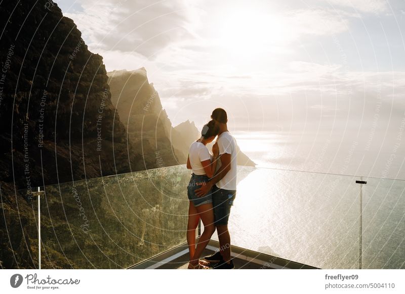Young couple on a viewpoint against volcanic cliffs and the ocean love honeymoon young sunset caucasian copy space rocks canary islands spain sea black sky trip