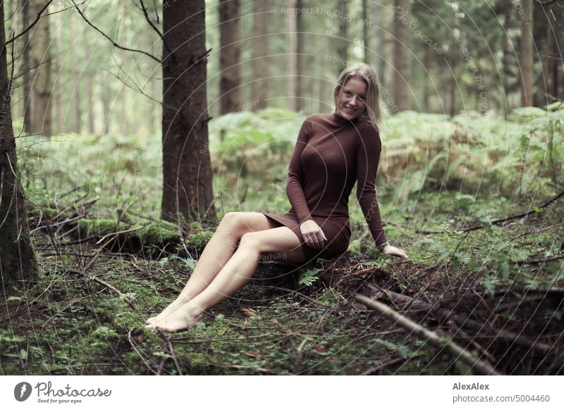 Young blonde woman sitting barefoot on fallen log in forest smiling at camera Young woman Woman Blonde Feminine pretty fortunate Youth (Young adults) portrait
