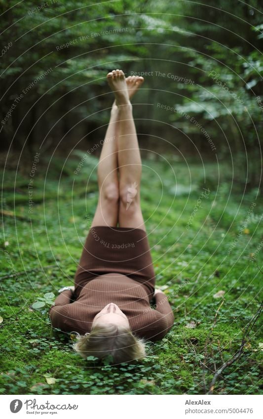 Young blonde woman lying barefoot in moss in on forest floor holding legs in air Young woman Woman Blonde Feminine pretty fortunate Youth (Young adults)
